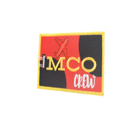 An embroidered rectangular patch with a yellow border, featuring a red and black background, a small red airplane silhouette, and the text 'MCO crew' in yellow and white.