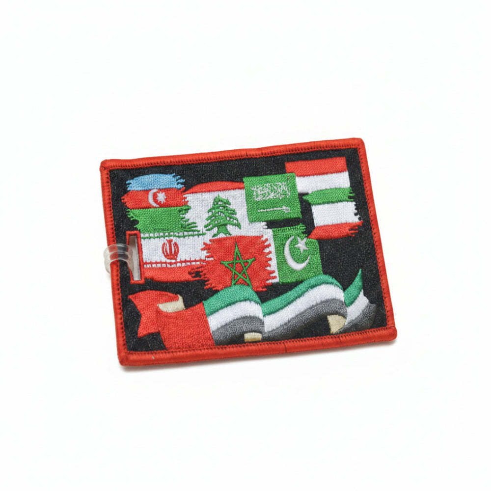 A rectangular embroidered patch featuring multiple flags, including Iran, Syria, Iraq, Lebanon, Saudi Arabia, Libya, Pakistan, and others, with a red border and a clear plastic loop attached on the left, set against a bright yellow background.